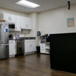 Image of an office breakroom with seating and a fridge, sink, coffee bar with wall art and nice lights.