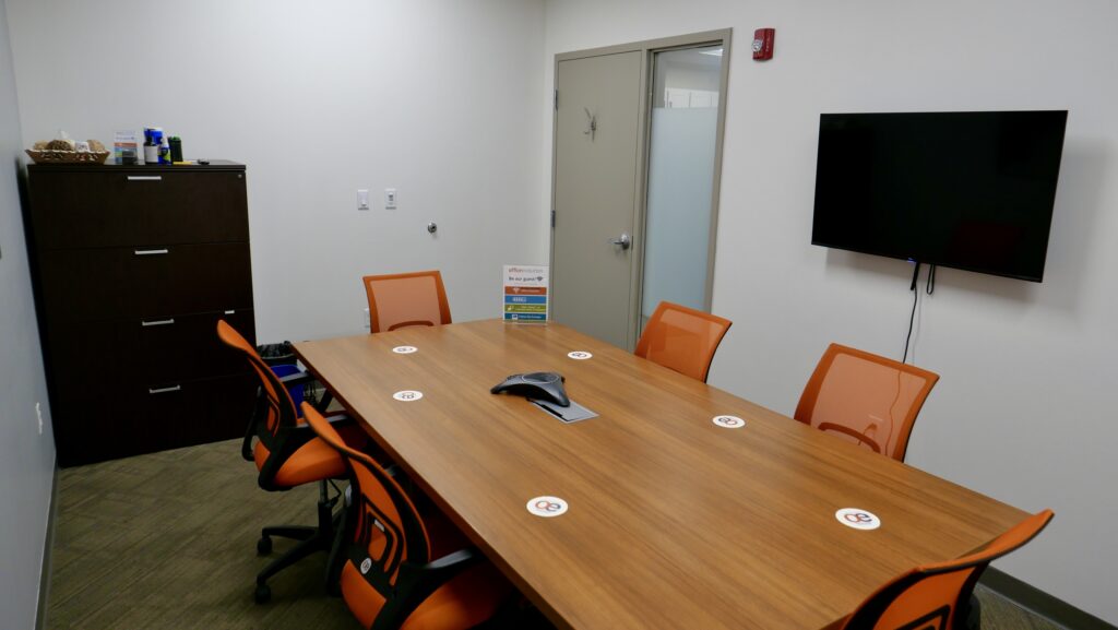 A medium sized Meeting room with orange colored seating and a phone for conference calls.