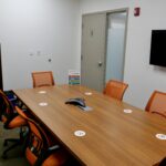 A medium sized Meeting room with orange colored seating and a phone for conference calls.