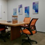 A medium sized meeting room space with colorful artwork on the wall and orange colored chairs.