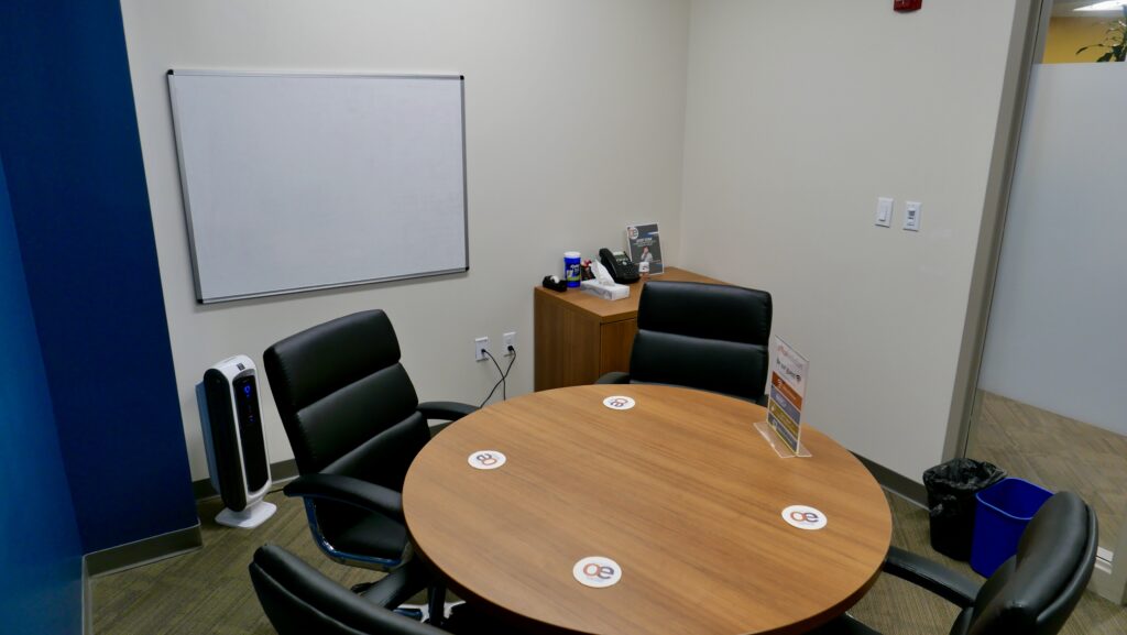 A small meeting room space with seating for 4x individuals and a whiteboard on the wall.