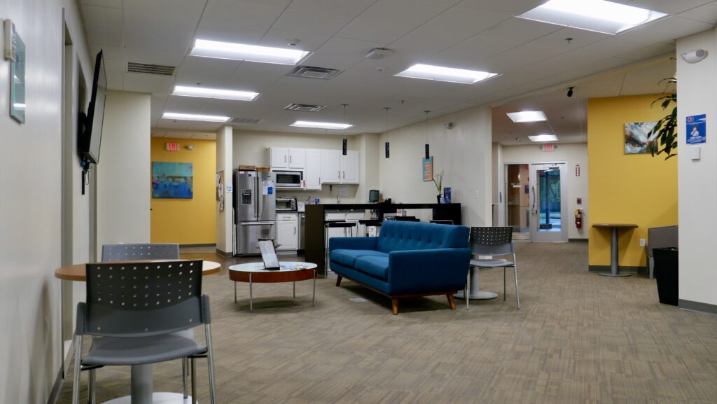 An office lobby area and break room with a blue couch and kitchen space. Lots of lighting.