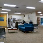 An office lobby area and break room with a blue couch and kitchen space. Lots of lighting.