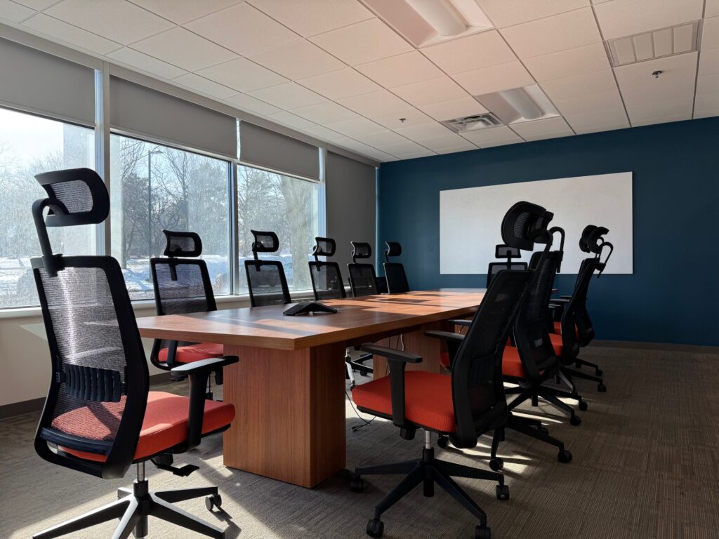 Photo of a sunny boardroom conference room with orange chairs and a blue wall with a big white board.