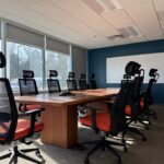 Photo of a sunny boardroom conference room with orange chairs and a blue wall with a big white board.