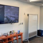 Image of a sizeable television flat screen and a wheel-mounted white board in a training room.