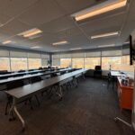 A large modern office training room space with seating for 30 people on rolling chairs. Room has sunny windows on two sides.