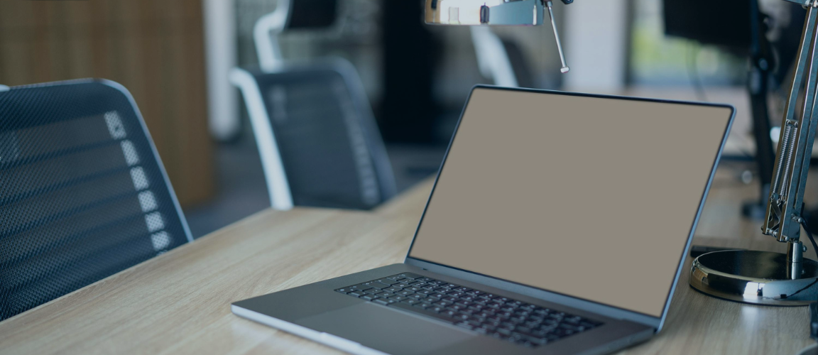 A laptop on a work desk with chairs in the back.